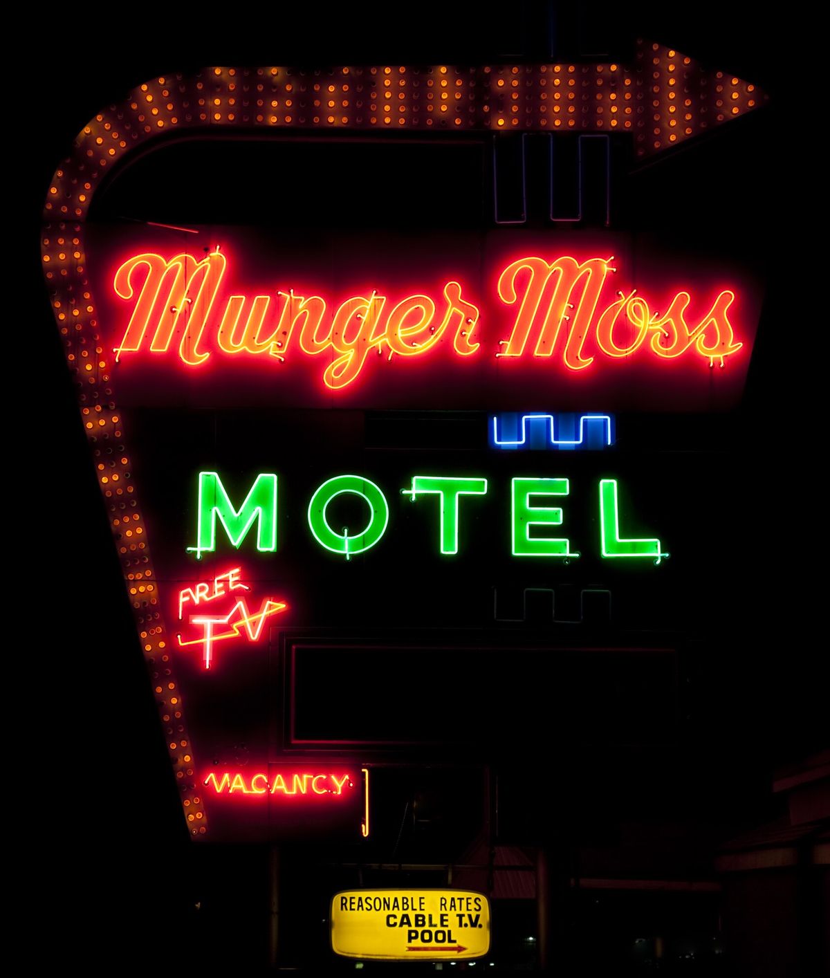 The Munger Moss Motel neon sign lit at night: yellow script, green MOTEL lettering and an arrow of amber bulbs